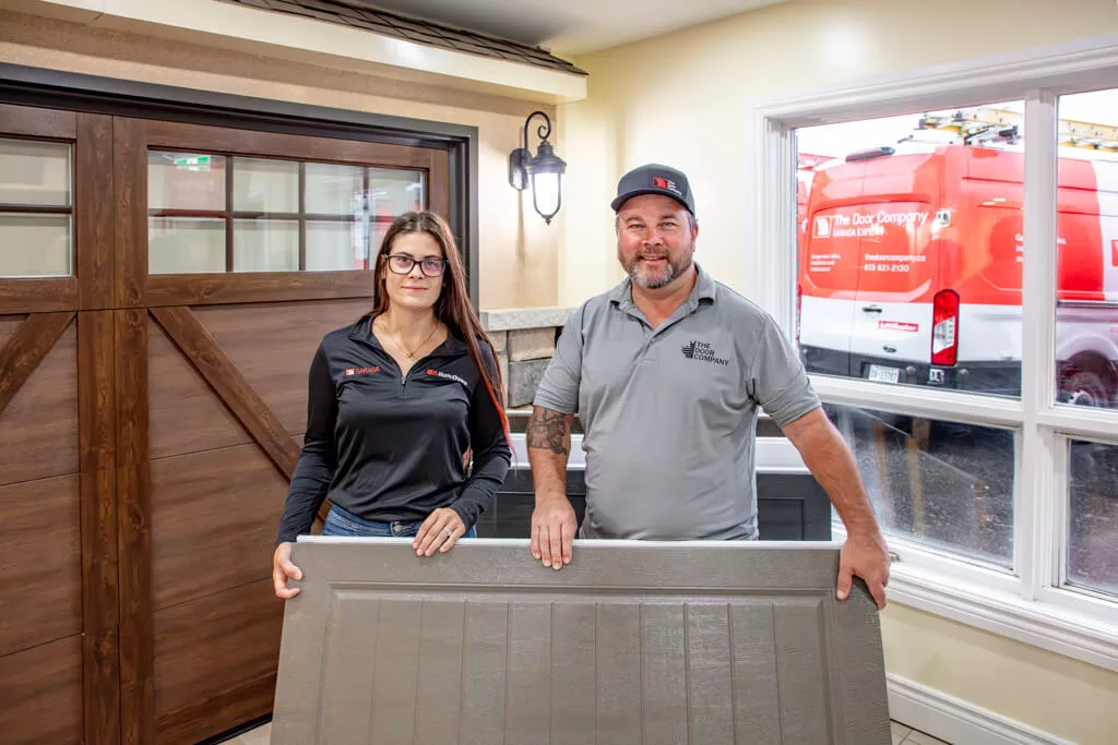 Two members of the Portes Ram Doors team in the showroom with a sample garage door ready to advise on your unique projet